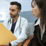 Médico conversa com paciente enquanto consulta registros de saúde em uma unidade clínica.
