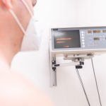 Paciente usando máscara é monitorado por equipamento eletrônico em uma clínica.