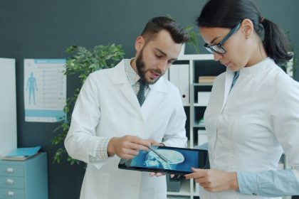 Médicos analisam uma radiografia exibida em um tablet durante atendimento em um consultório.