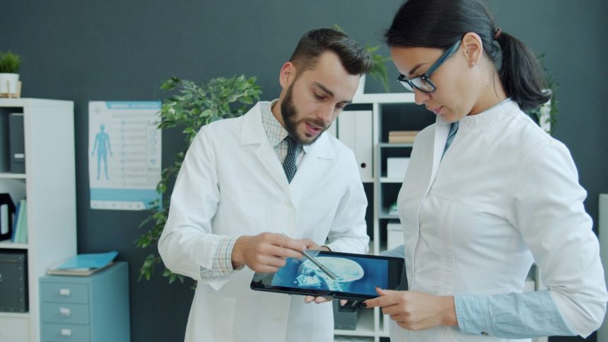 Médicos analisam uma radiografia exibida em um tablet durante atendimento em um consultório.