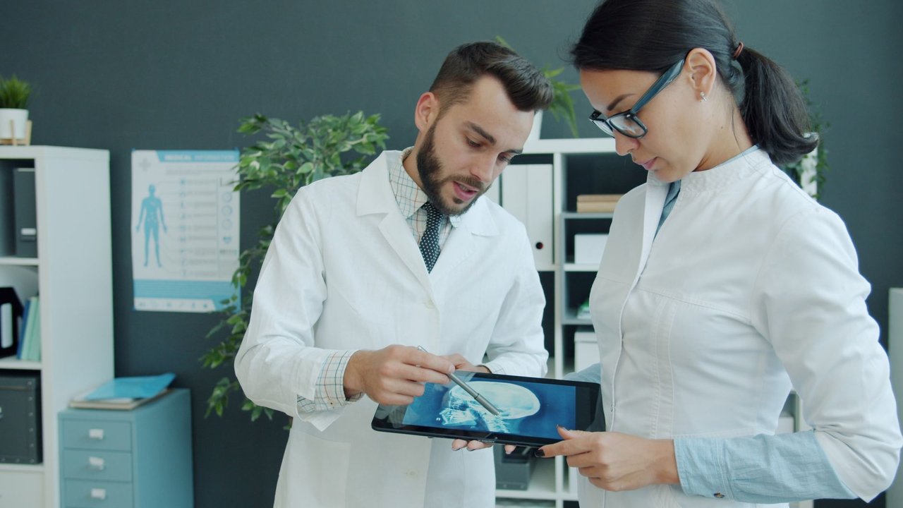 Médicos analisam uma radiografia exibida em um tablet durante atendimento em um consultório.
