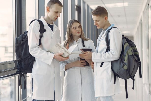 Três estudantes de medicina conversam e consultam anotações em um corredor hospitalar.
