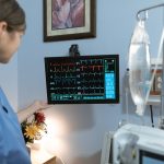 Profissional de enfermagem observa um monitor de sinais vitais em uma unidade hospitalar.