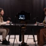 Dois apresentadores gravam um podcast em um estúdio equipado com microfones e outros aparelhos profissionais.