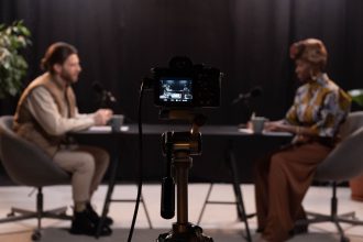 Dois apresentadores gravam um podcast em um estúdio equipado com microfones e outros aparelhos profissionais.